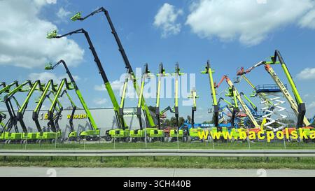 Sollevatori a braccio e sollevatori a forbice esposti in un'azienda di noleggio di attrezzature pesanti sotto un cielo blu. Polonia - 19 agosto 2025 Foto Stock