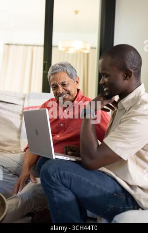 Nonno e nipote che usano il laptop insieme a casa, condividendo momenti di gioia Foto Stock