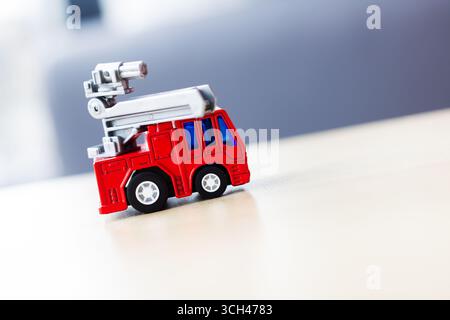 Un vivace camion rosso giocattolo del fuoco con una scala si trova su un tavolo di legno, perfetto per giochi e decorazioni fantasiose. Foto Stock