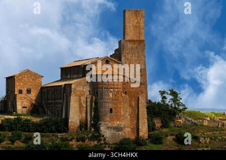 Le torri di avvistamento medievali si innalzano sopra i tetti piastrellati della basilica romanica lombarda di San Pietro o San Pietro, un'ex cattedrale costruita sulla sommità dell'antica acropoli etrusca a Tuscania, Lazio, Italia. La navata e la caratteristica abside arrotondata sono state ritenute innovazioni dell'VIII secolo, ma gli storici dell'architettura moderna credono che possano essere da 200 a 300 anni più giovani. Foto Stock