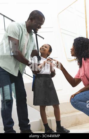 padre e madre incoraggiano la figlia in uniforme scolastica sulle scale a casa Foto Stock