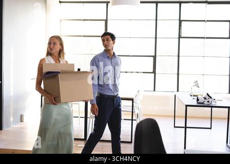 Colleghi che trasportano la scatola e camminano in un ufficio moderno, discutendo di un nuovo progetto Foto Stock