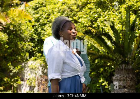 Donna afroamericana che gode di una giornata di sole in giardino, sorridente e dall'aspetto accattivante Foto Stock
