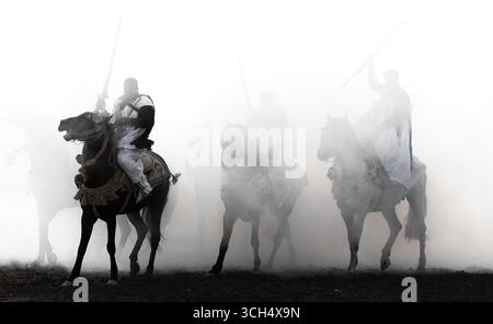 Una storia di coraggio, unità e eredità catturata in un unico fotogramma.Riders in colorati costumi marocchini al galoppo su cavalli arabi in uno spettacolo Fantasia Foto Stock