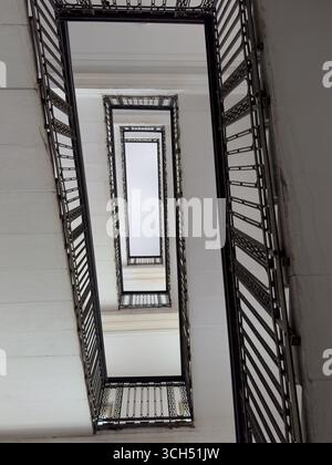 Si affaccia su una scala moderna con intricate ringhiere in metallo, che mostrano design architettonico e simmetria. Foto Stock