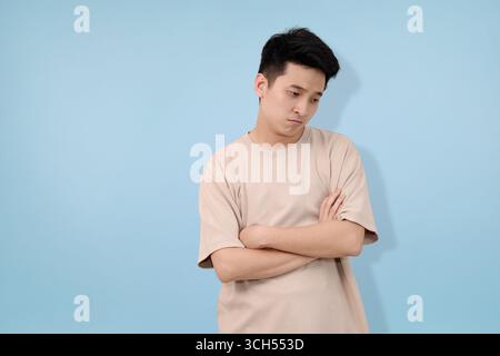 il giovane mostra un'espressione preoccupante con le braccia incrociate su un solido sfondo blu Foto Stock