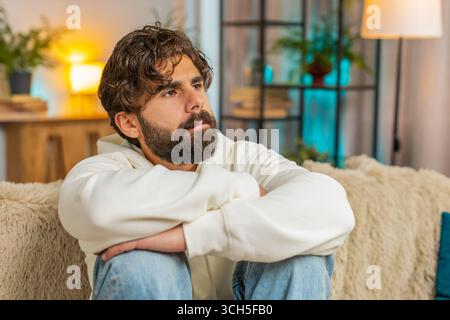 Un giovane indiano triste e frustrato, seduto a casa, sembra penoso pensare alla vita solitaria o ai problemi, alla crisi, soffre di una situazione ingiusta. Malattia, anx Foto Stock