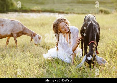 Giovane agricoltore che si prende cura delle capre sul prato verde all'ora d'oro, ideale per il latte di capra l'agricoltura biologica e l'agriturismo Foto Stock