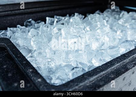 Vista ravvicinata di un contenitore riempito di cubetti di ghiaccio trasparente, che mostra la loro consistenza congelata e la freschezza fredda Foto Stock