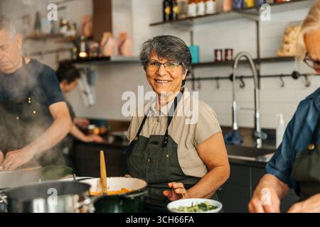 Ritratto di una studentessa anziana non tradizionale dai capelli corti sorridente che impara in una lezione di cucina in una cucina commerciale Foto Stock