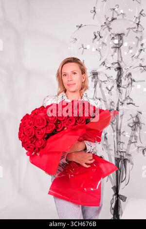 mosca, russia, 24.06.2025 donne con un grande bouquet di rose rosse avvolte in carta rossa con palloncini trasparenti dietro di lei durante le festività natalizie Foto Stock