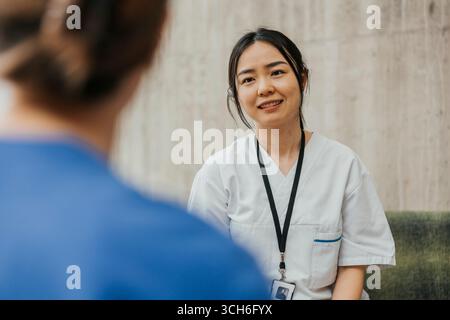 Infermiera donna che indossa scrub medico che parla con il collega nella hall dell'ospedale Foto Stock