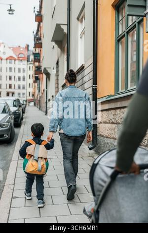 Vista posteriore della madre che tiene per mano il figlio mentre cammina sul marciapiede Foto Stock