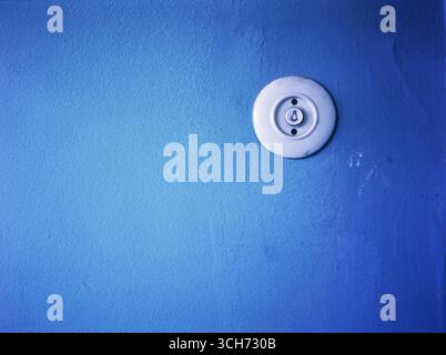 Una fotografia ravvicinata di un vecchio bottone del campanello montato su una parete blu testurizzata all'interno di un edificio residenziale. Foto Stock