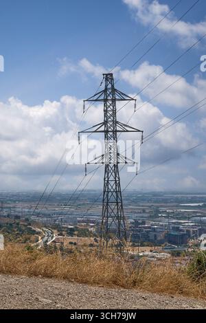 Una torre ad alta tensione è l'elemento centrale di questo paesaggio, con l'area urbana di Viladecans, edifici industriali e campi visibili Foto Stock