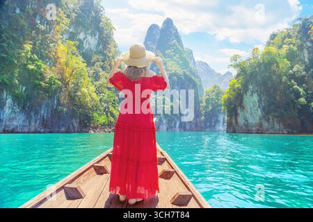 Una donna viaggiatrice da sola gode delle viste mozzafiato del lago Cheow LAN, circondato da torreggianti scogliere calcaree e da una vegetazione lussureggiante a Khao Sok, in Tailandia Foto Stock