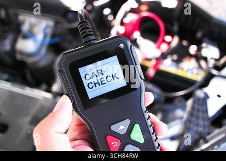 Mano che tiene in mano uno scanner diagnostico per auto OBD2 con schermo che visualizza il controllo della vettura, utilizzato per la manutenzione del veicolo, la lettura dei codici di errore del motore e il settore automobilistico Foto Stock