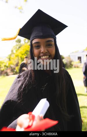 Studente laureato in cappello e abito sorridente e in possesso di diploma in giardino Foto Stock