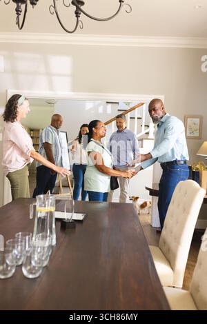 Riuniti a casa, diversi amici anziani accolgono calorosamente gli ospiti con sorrisi e strette di mano. celebrazione, ospitalità, interazione, accoglienza, insieme Foto Stock