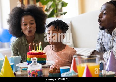 Alla festa, festeggiando il compleanno, una famiglia di tre persone che soffiano candele su una torta colorata a casa Foto Stock