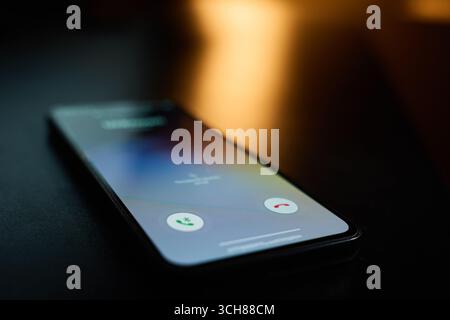 Primo piano di uno smartphone appoggiato sul tavolo in una stanza buia con le chiamate in arrivo sullo schermo. Concetto di comunicazione, tecnologia e connessione mobile Foto Stock