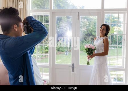 La sposa regge il bouquet in posa per il fotografo in una stanza luminosa ed elegante Foto Stock