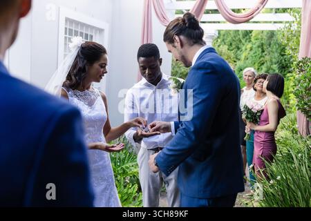 Sposa e sposo si scambiano anelli all'aperto, circondati da amici e familiari Foto Stock