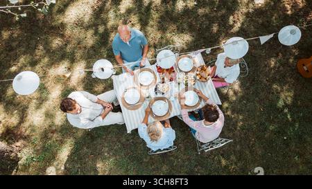 Vista aerea dei nonni, dei genitori e dei bambini che mangiano insieme all'esterno. Foto Stock