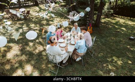 Vista aerea dei nonni, dei genitori e dei bambini che mangiano insieme all'esterno. Foto Stock