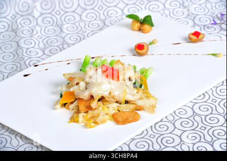 Sea Whelk fritto in padella con funghi misti su piatto bianco Foto Stock