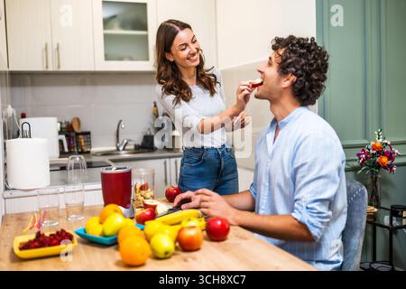 Una giovane coppia che condivide un divertente momento di cottura, preparando frullati di frutta sani con un mixer elettrico. Foto Stock