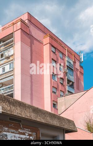 Alto edificio residenziale con pareti e finestre in cemento rosa usurate in una giornata di sole. Messa a fuoco selettiva. Foto Stock