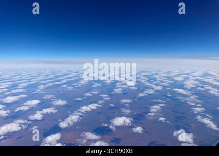 Nuvole soffici sparse di colore bianco con motivo che scompaiono verso l'orizzonte proiettano ombre sulla terra rossa dell'Australia centrale direttamente sotto, viste attraverso l'aereo wi Foto Stock