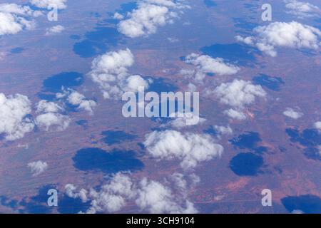 Nuvole soffici sparse bianche gettano ombre sulla terra rossa dell'Australia centrale direttamente sotto, vista dalla finestra dell'aereo. Foto Stock
