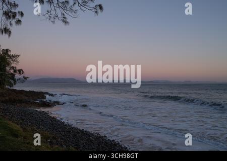 Onde delicate che lavano la spiaggia di ciottoli al crepuscolo con il cielo rosa Foto Stock