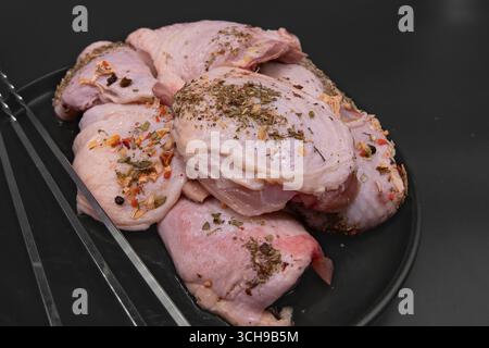 Cosce di pollo crude fresche con una pelle cosparsa di spezie ed erbe aromatiche con spiedini di metallo pronti per grigliare barbecue e preparare la cottura Foto Stock