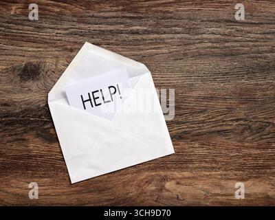 Aprire la busta contenente una scheda con la scritta aiuto, appoggiata su una superficie di legno. Richiesta di assistenza e supporto. Foto Stock