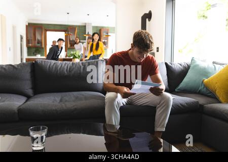 Teen che legge la lettera di accettazione del college mentre gli amici festeggiano in salotto, a casa, spazio di copia. festeggiamenti, adolescente, felicità, casa, al chiuso, s Foto Stock
