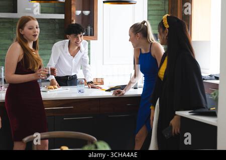 Diversi adolescenti che celebrano la laurea in cucina, ridono e bevono un drink insieme, a casa. Festeggiamenti, adolescenti diversi, amicizia, festa, a.. Foto Stock