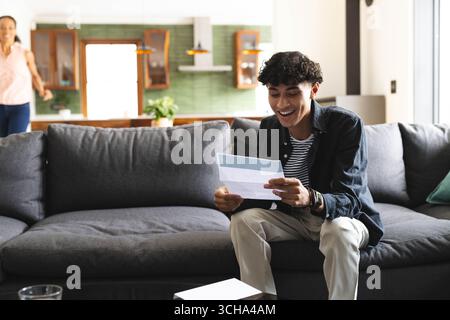 Teen che legge la lettera di accettazione del college sul divano, sorride di eccitazione a casa, copia spazio. Felice, gioioso, rilassante, confortevole, accogliente, tempo libero Foto Stock