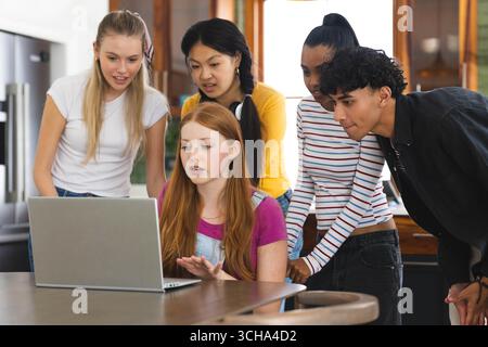 Guardare lo schermo di un notebook in cucina, i vari adolescenti che condividono momenti di gioia a casa. amici diversi, legame, tecnologia, tempo libero, felicità Foto Stock