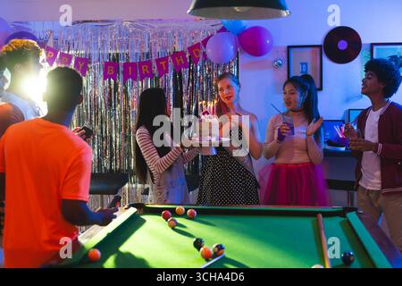 Diversi amici adolescenti festeggiano il compleanno con torta e bevande intorno al tavolo da biliardo alla festa, a casa. Festeggiamenti, amici adolescenti diversi, compleanno Foto Stock