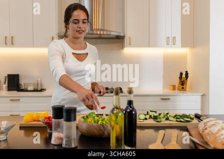 Donna che prepara insalata fresca in cucina moderna, sorride e si diverte a cucinare, copiare spazio, a casa. cucina, sano, stile di vita, verdure, casa, pasto Foto Stock