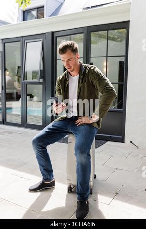 Uomo seduto in valigia all'aperto, che controlla lo smartphone, che si prepara al viaggio. viaggio, vacanza, avventura, trasporto, cellulare, bagagli Foto Stock