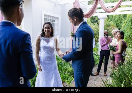 Sposa e sposo si scambiano le promesse all'aperto, circondati da amici e familiari gioiosi. Matrimonio, cerimonia, celebrazione, amore, impegno, coppia Foto Stock