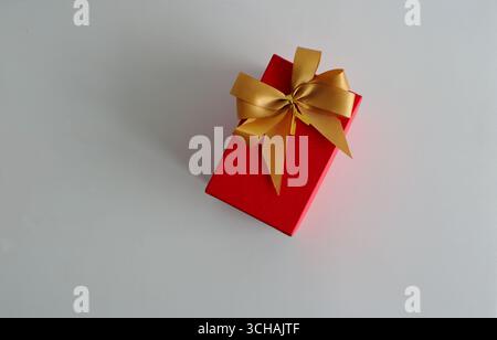 Vista ad angolo alto della scatola rossa con arco dorato posizionato su un tavolo di legno bianco Foto Stock