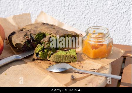 Torta rustica di spinaci senza glutine con prugne e marmellata di albicocche fatta in casa, esposta con coltello e cucchiaio su un asse di legno. Dolce fatto in casa sano Foto Stock
