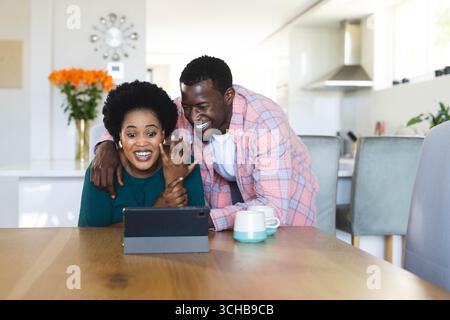 Coppia che mostra il coinvolgimento squilla durante una videochiamata nella moderna cucina domestica, con laptop.contemporaneo, gioioso, intimo, elegante, stile di vita accogliente e vivace. Foto Stock
