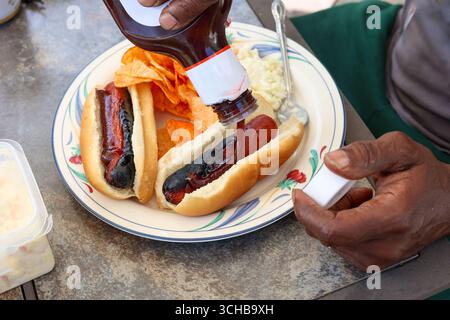 Un Black Man che versa salsa barbecue su Un Hotdog Foto Stock