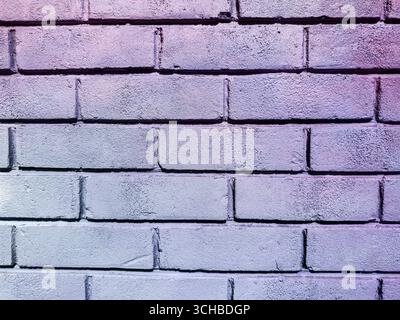 Primo piano di una parete in mattoni dipinti a pastello con sfumatura viola e superficie ruvida, ideale per sfondi, lavori di progettazione o progetti creativi. Foto Stock